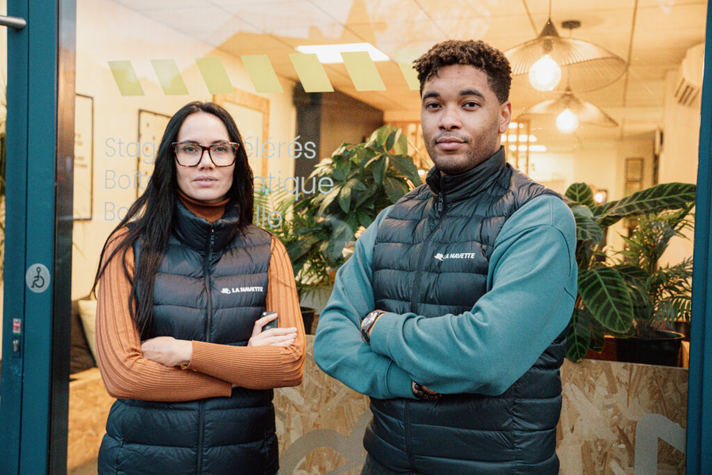 Deux membres de l’équipe La Navette posant devant les locaux de l’auto-école, habillés en doudoune logotypée.